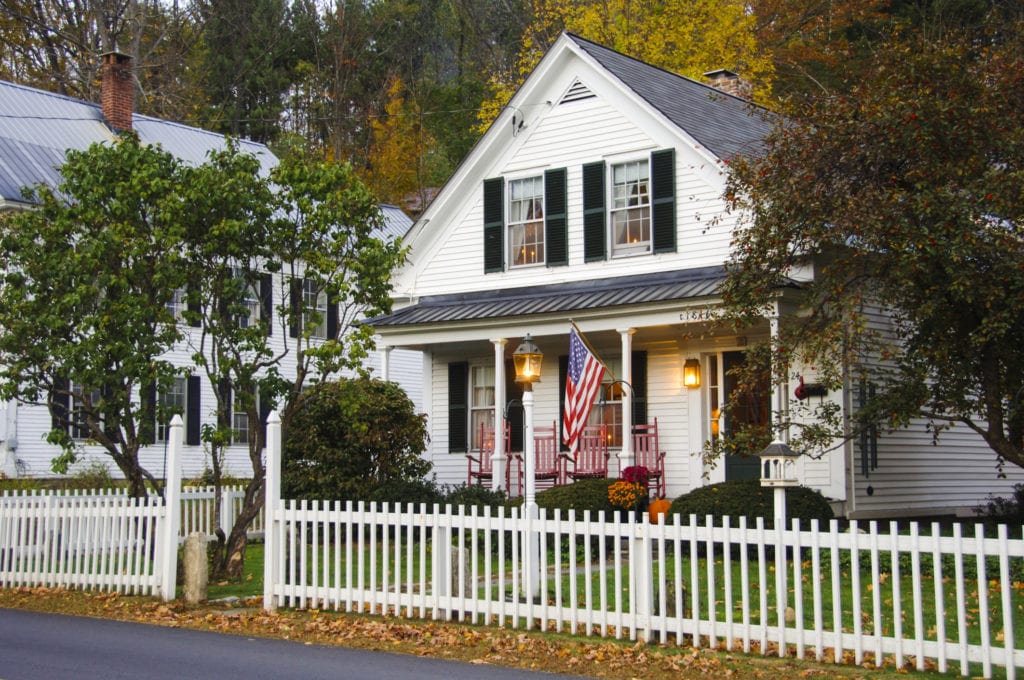photo of a house with a white picket fence and american flag in the fall